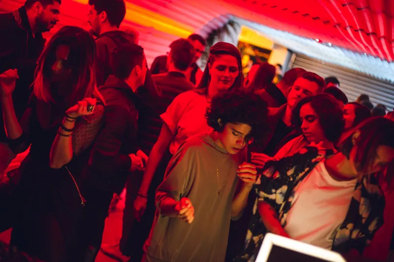 Dance floor bathed in red light at Vortex, the crowd moving under a corrugated roof.