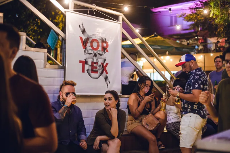 The Vortex banner — the name in red over an engraved skull — hanging by a staircase while people talk and drink around it.