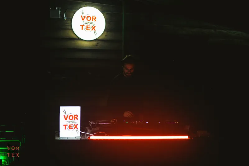 Dark Vortex stage: the round illuminated logo above the booth and a red neon tube glowing over the decks.